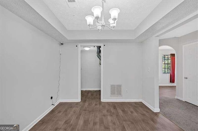 unfurnished room featuring a raised ceiling, dark hardwood / wood-style floors, a textured ceiling, and an inviting chandelier