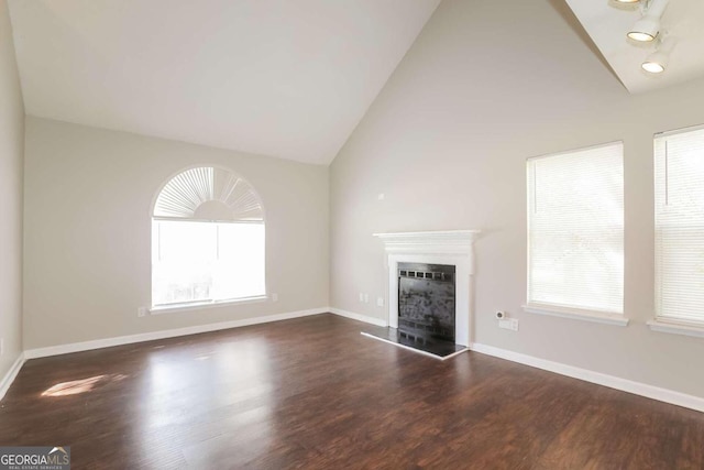 unfurnished living room featuring a healthy amount of sunlight, dark wood-type flooring, and high vaulted ceiling