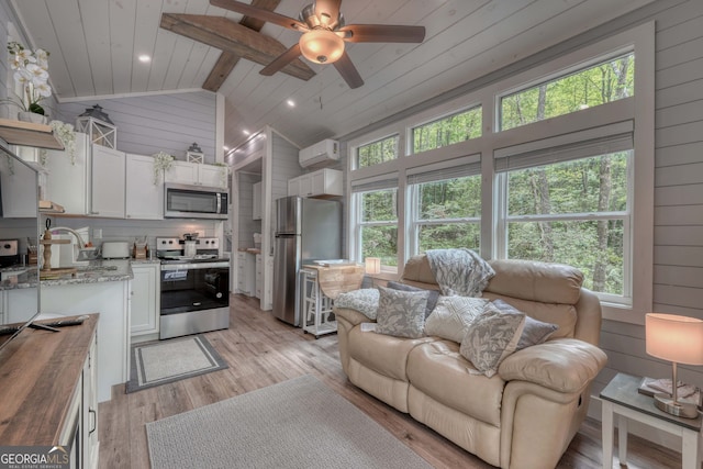 living room featuring lofted ceiling, ceiling fan, wooden walls, a wall mounted AC, and light wood-type flooring