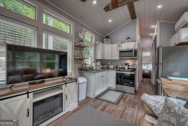 kitchen featuring appliances with stainless steel finishes, lofted ceiling with beams, dark stone countertops, white cabinets, and light hardwood / wood-style flooring