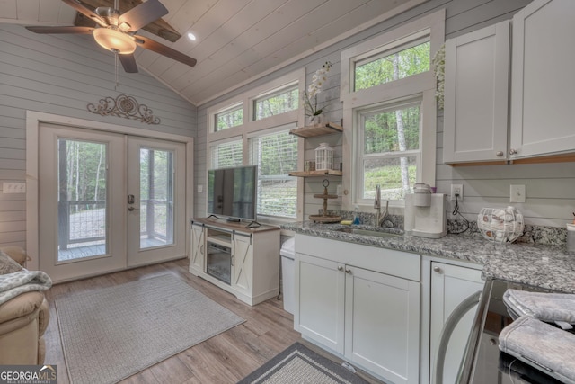 kitchen featuring sink, white cabinetry, light stone counters, vaulted ceiling, and light wood-type flooring