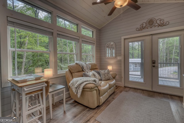 living area featuring lofted ceiling, ceiling fan, wooden walls, light hardwood / wood-style floors, and french doors