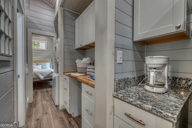 kitchen featuring white cabinetry, light stone counters, light hardwood / wood-style flooring, and wooden walls