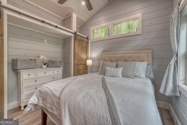 bedroom with vaulted ceiling, a barn door, ceiling fan, and light hardwood / wood-style floors