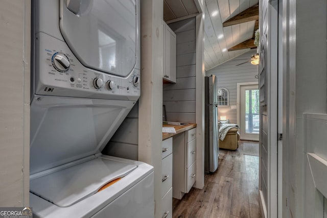 laundry room with ceiling fan, stacked washer and clothes dryer, light hardwood / wood-style floors, and wood walls