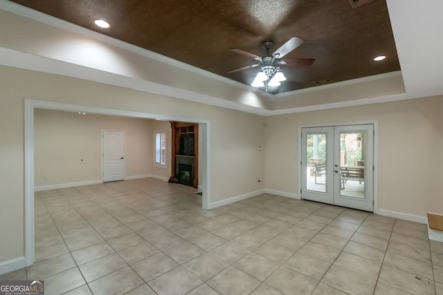 empty room with french doors, a tray ceiling, light tile patterned floors, and ceiling fan