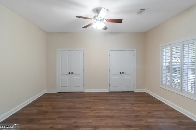 unfurnished bedroom with ceiling fan, dark wood-type flooring, and two closets