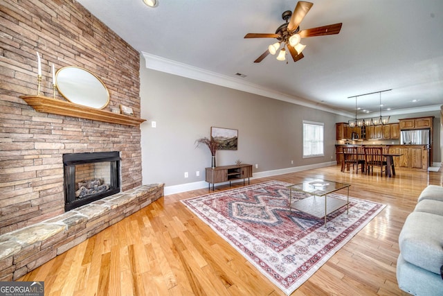 living room featuring a stone fireplace, ceiling fan, light hardwood / wood-style floors, and ornamental molding