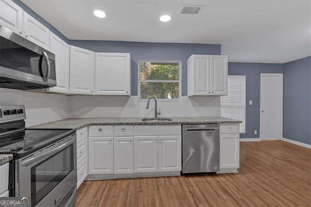 kitchen featuring appliances with stainless steel finishes, light stone counters, sink, light hardwood / wood-style floors, and white cabinetry