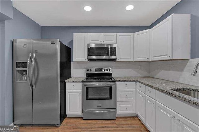 kitchen with light stone countertops, stainless steel appliances, sink, hardwood / wood-style floors, and white cabinetry