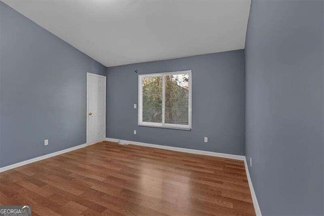 empty room with hardwood / wood-style floors and vaulted ceiling