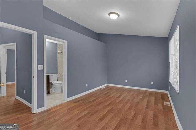 unfurnished bedroom featuring wood-type flooring and connected bathroom