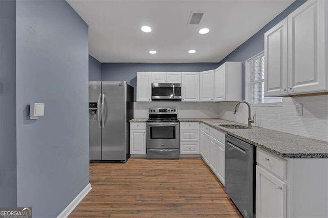 kitchen featuring white cabinets, sink, light wood-type flooring, appliances with stainless steel finishes, and light stone counters