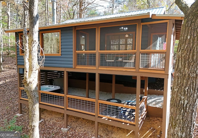 back of house featuring metal roof, log veneer siding, and a sunroom