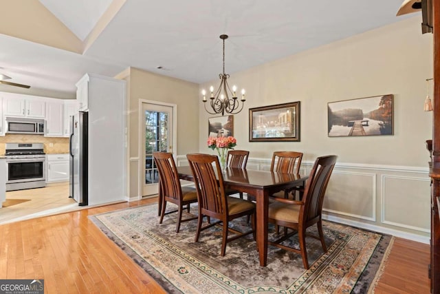 dining room with ceiling fan with notable chandelier, vaulted ceiling, and light wood-type flooring