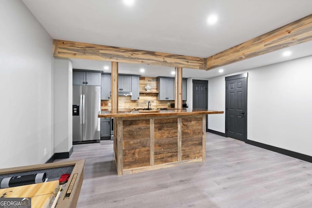 kitchen with gray cabinetry, a center island, stainless steel refrigerator with ice dispenser, wood-type flooring, and decorative backsplash