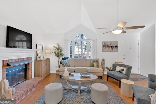 living room with ceiling fan, a brick fireplace, lofted ceiling, and light wood-type flooring