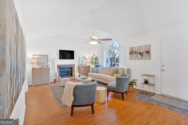 living room featuring lofted ceiling, a brick fireplace, light hardwood / wood-style floors, and ceiling fan