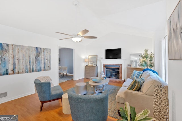 living room featuring ceiling fan, a fireplace, vaulted ceiling, and light hardwood / wood-style flooring