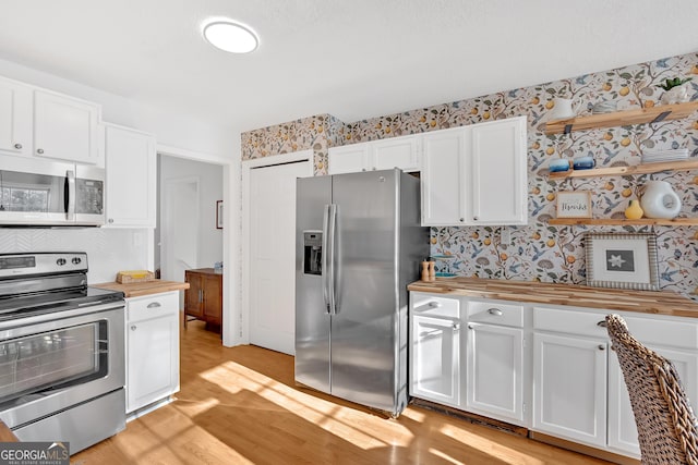 kitchen featuring wooden counters, appliances with stainless steel finishes, white cabinets, and light wood-type flooring