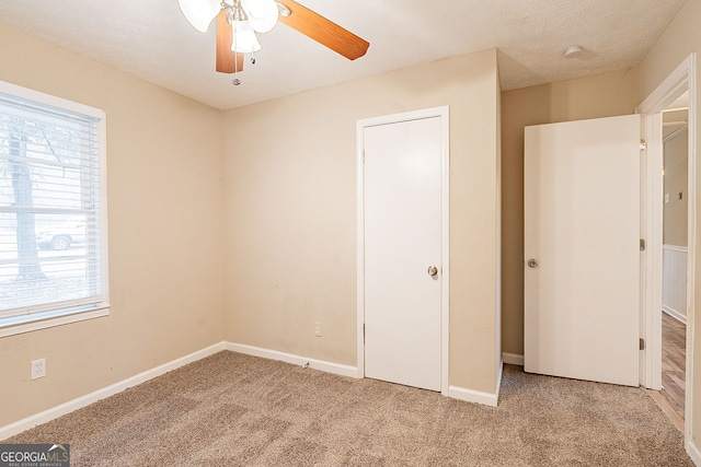 unfurnished bedroom with a textured ceiling, ceiling fan, light carpet, and multiple windows