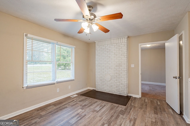 empty room featuring hardwood / wood-style floors, ceiling fan, a textured ceiling, and brick wall