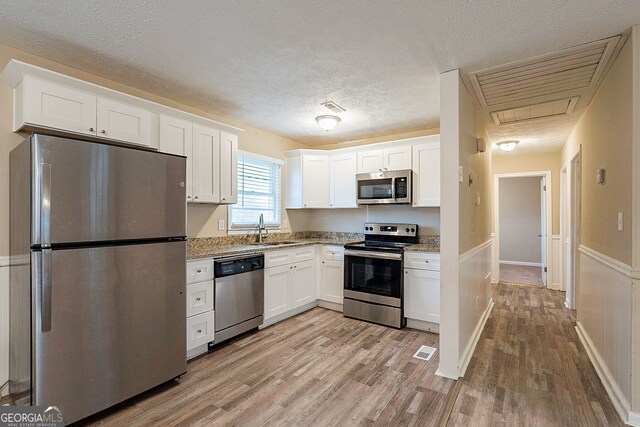 kitchen with a textured ceiling, stainless steel appliances, sink, light hardwood / wood-style floors, and white cabinetry