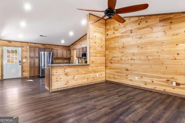 kitchen featuring kitchen peninsula, appliances with stainless steel finishes, dark hardwood / wood-style flooring, vaulted ceiling, and wooden walls