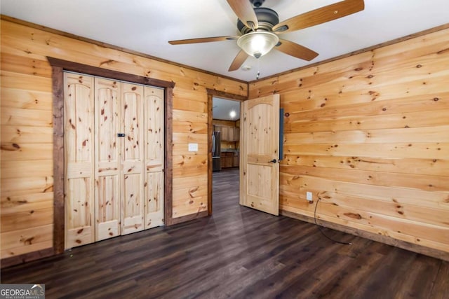 unfurnished bedroom with wooden walls, refrigerator, dark wood-type flooring, and ceiling fan