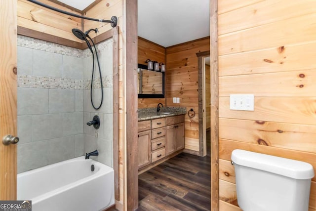 full bathroom featuring vanity, hardwood / wood-style floors, toilet, tiled shower / bath, and wood walls