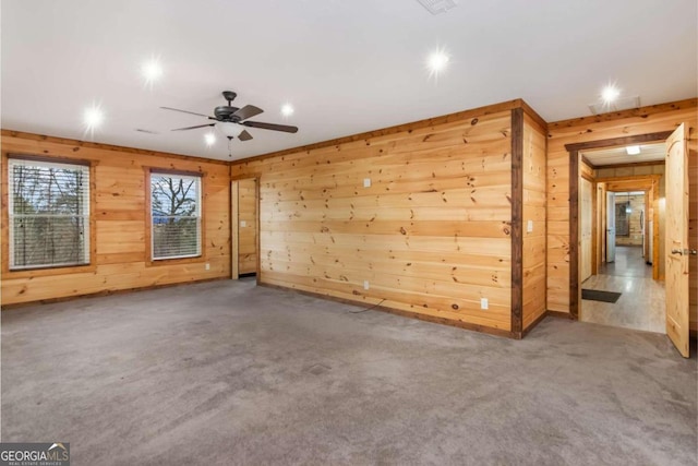 unfurnished room with carpet flooring, ceiling fan, and wooden walls