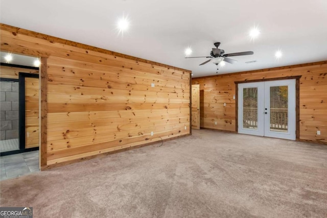 unfurnished living room with ceiling fan, carpet floors, wooden walls, and french doors