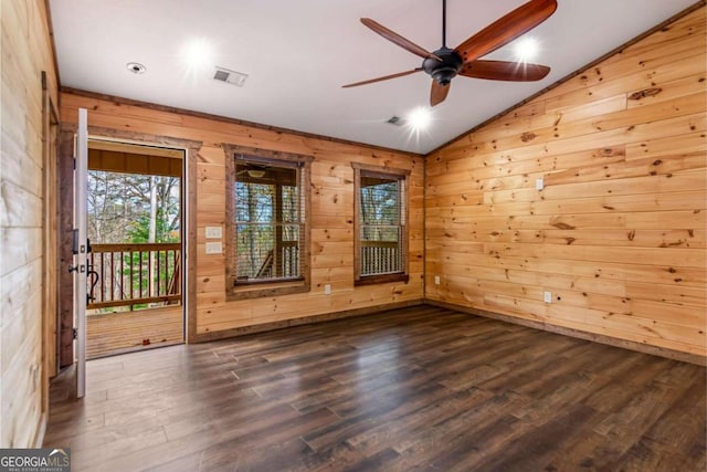 spare room featuring vaulted ceiling, ceiling fan, dark wood-type flooring, and wood walls