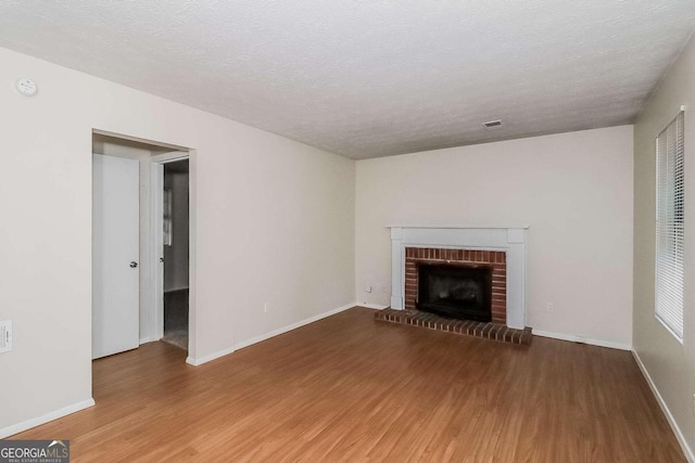 unfurnished living room with a brick fireplace, a textured ceiling, and hardwood / wood-style flooring