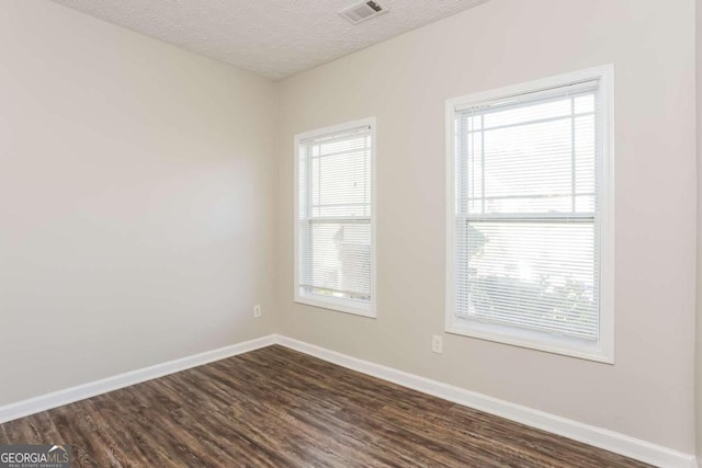 empty room featuring a healthy amount of sunlight, dark hardwood / wood-style flooring, and a textured ceiling