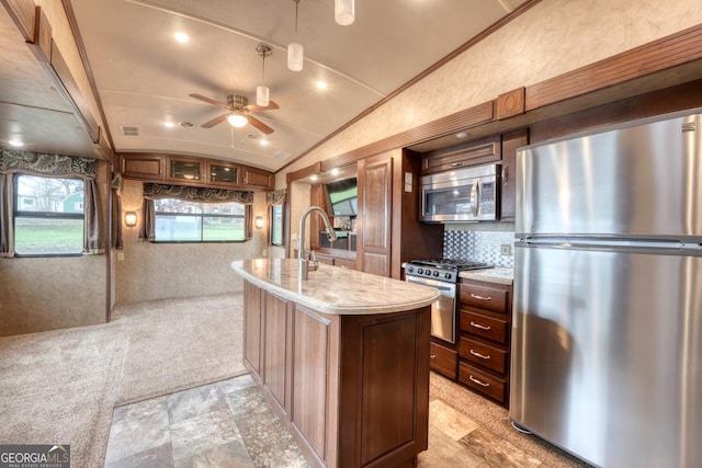 kitchen featuring lofted ceiling, an island with sink, ceiling fan, stainless steel appliances, and light stone countertops