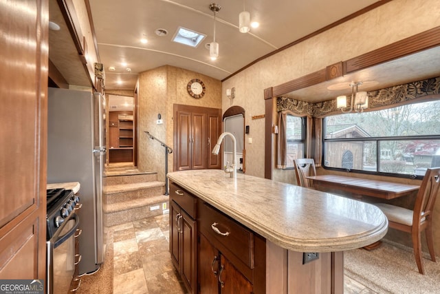 kitchen featuring an island with sink, pendant lighting, stainless steel gas range, and crown molding