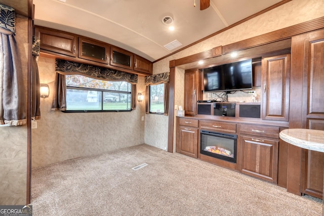 kitchen with carpet floors, visible vents, glass insert cabinets, ornamental molding, and vaulted ceiling