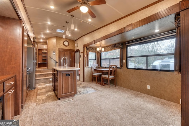 kitchen with arched walkways, light countertops, freestanding refrigerator, light carpet, and a kitchen island with sink