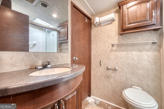 bathroom with stone finish floor, visible vents, vanity, and toilet