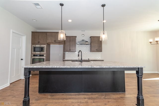 kitchen with appliances with stainless steel finishes, light stone counters, a kitchen island with sink, and sink