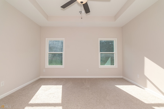 carpeted spare room with a raised ceiling and ceiling fan