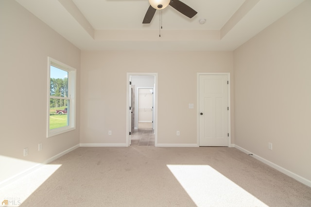 unfurnished bedroom with a raised ceiling, light carpet, and ceiling fan