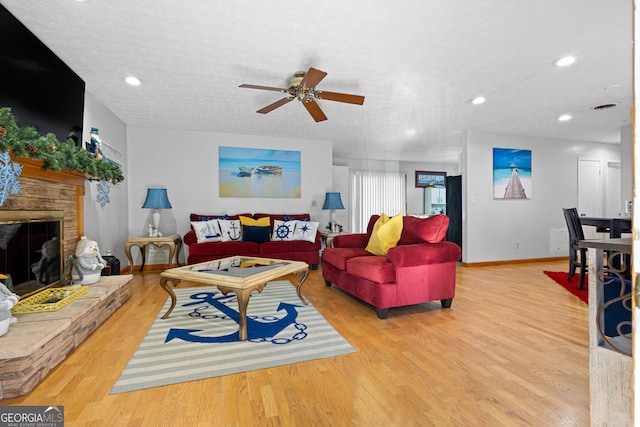 living room with a stone fireplace, ceiling fan, a textured ceiling, and light wood-type flooring