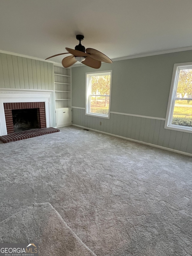 unfurnished living room featuring carpet, ceiling fan, built in features, and a brick fireplace