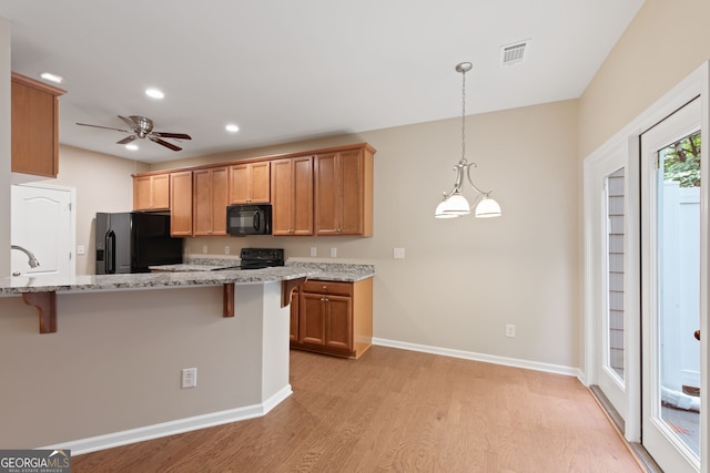 kitchen with a breakfast bar area, light stone countertops, light hardwood / wood-style flooring, and black appliances