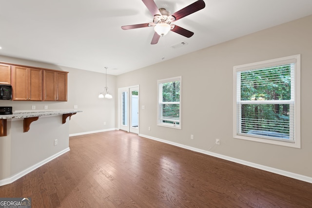 unfurnished living room featuring ceiling fan with notable chandelier and dark hardwood / wood-style floors