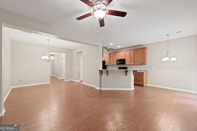 kitchen with a breakfast bar, pendant lighting, light hardwood / wood-style floors, and ceiling fan with notable chandelier