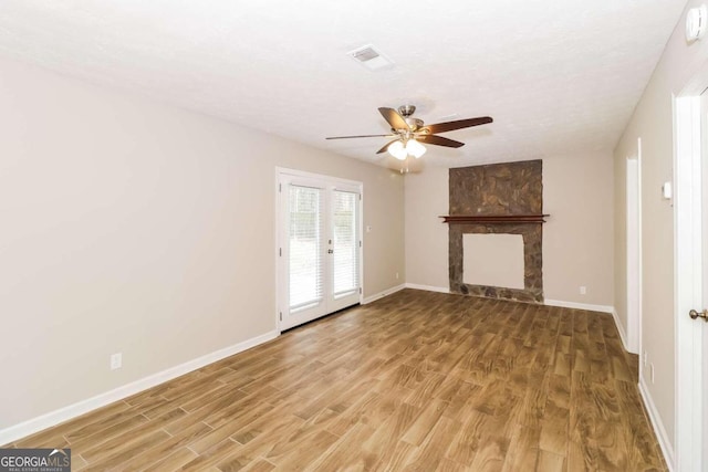 unfurnished living room with french doors, ceiling fan, a textured ceiling, a fireplace, and wood-type flooring