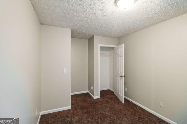 unfurnished bedroom featuring dark colored carpet, a textured ceiling, and a closet